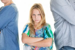 Unhappy girl standing between divorcing father and mother